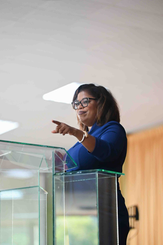 Ms. Delamae Wilson delivering a keynote address from a clear podium at an event.