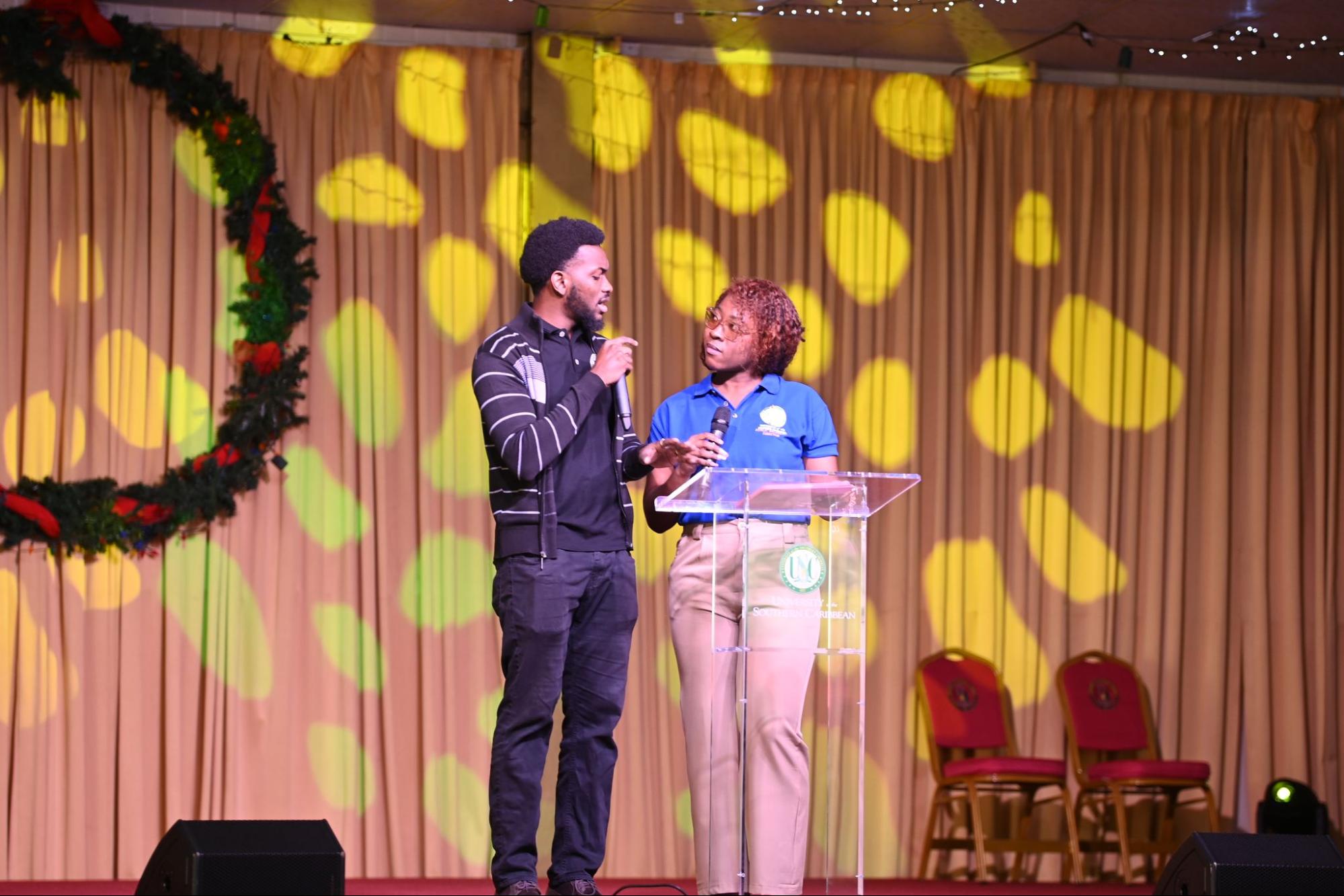 Michael Garcia and Hannah Walcott on stage as hosts of the USC January 2026 Orientation, speaking into microphones next to a clear podium.