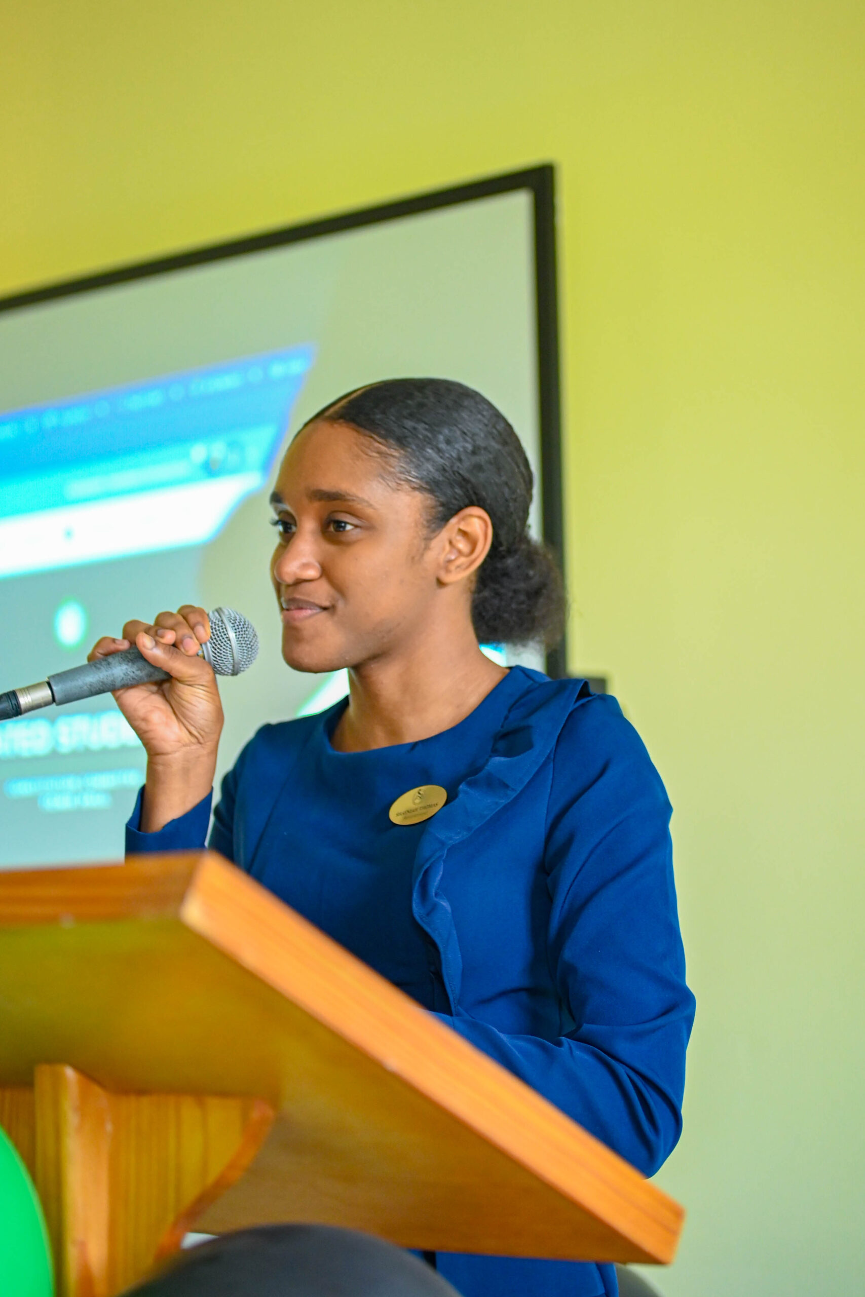 Parliamentarian Shayniah Thomas speaks into a microphone behind a wooden podium decorated with green and black balloons.