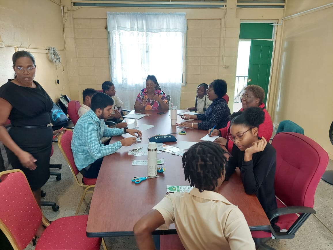 University of the Southern Caribbean pre-service teachers and San Juan North Secondary School students engage in a collaborative literacy workshop around a large table as part of the Bridges to Excellence initiative.