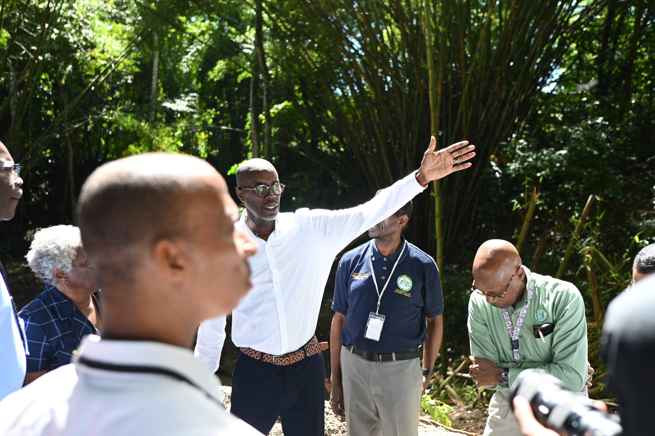 Mr. Arthur gestures towards a wooded area while speaking to a group of university officials and trustees on a nature trail