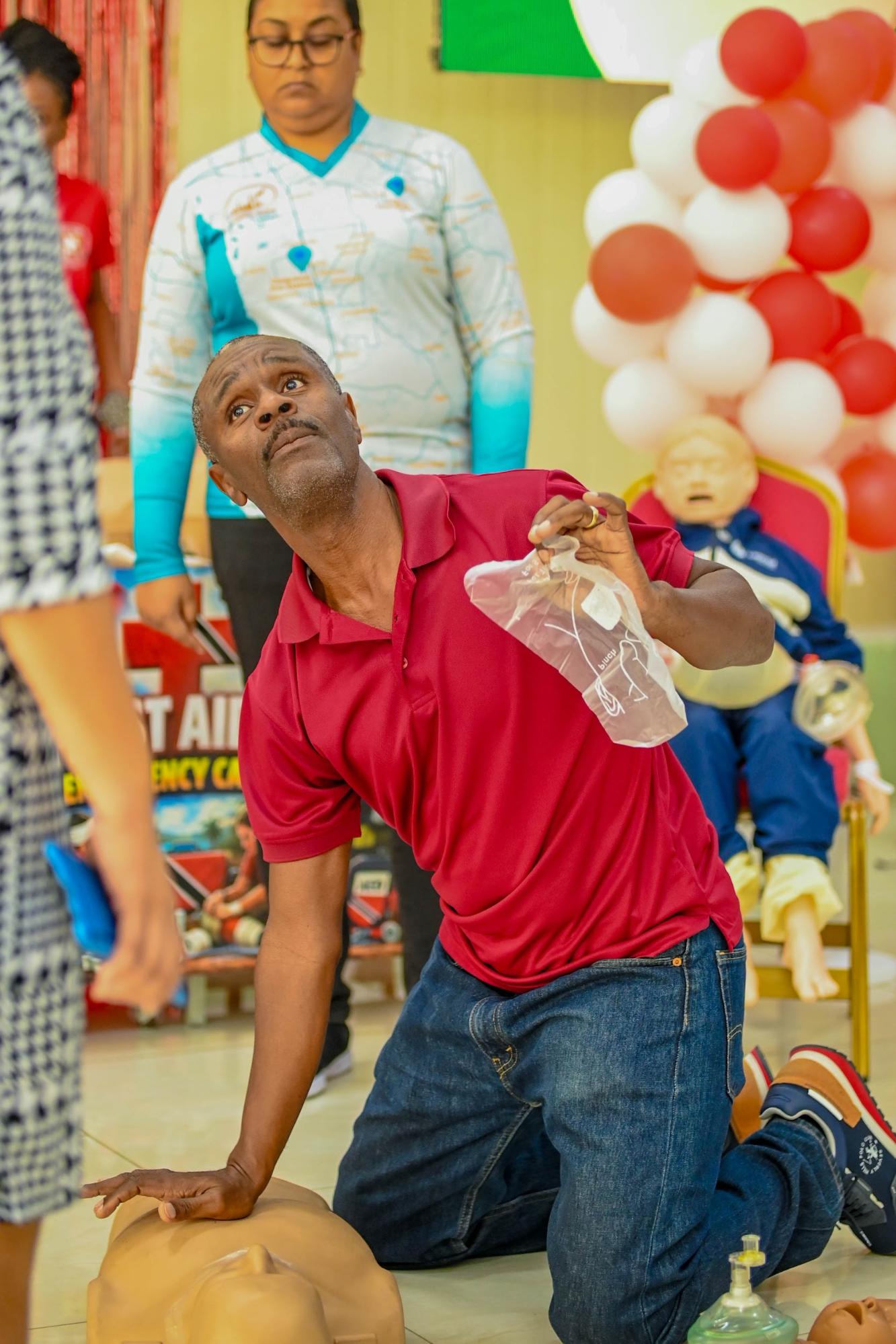 A male instructor demonstrates CPR on a training dummy during a health and wellness outreach programme for the University of the Southern Caribbean AOK-100 initiative.