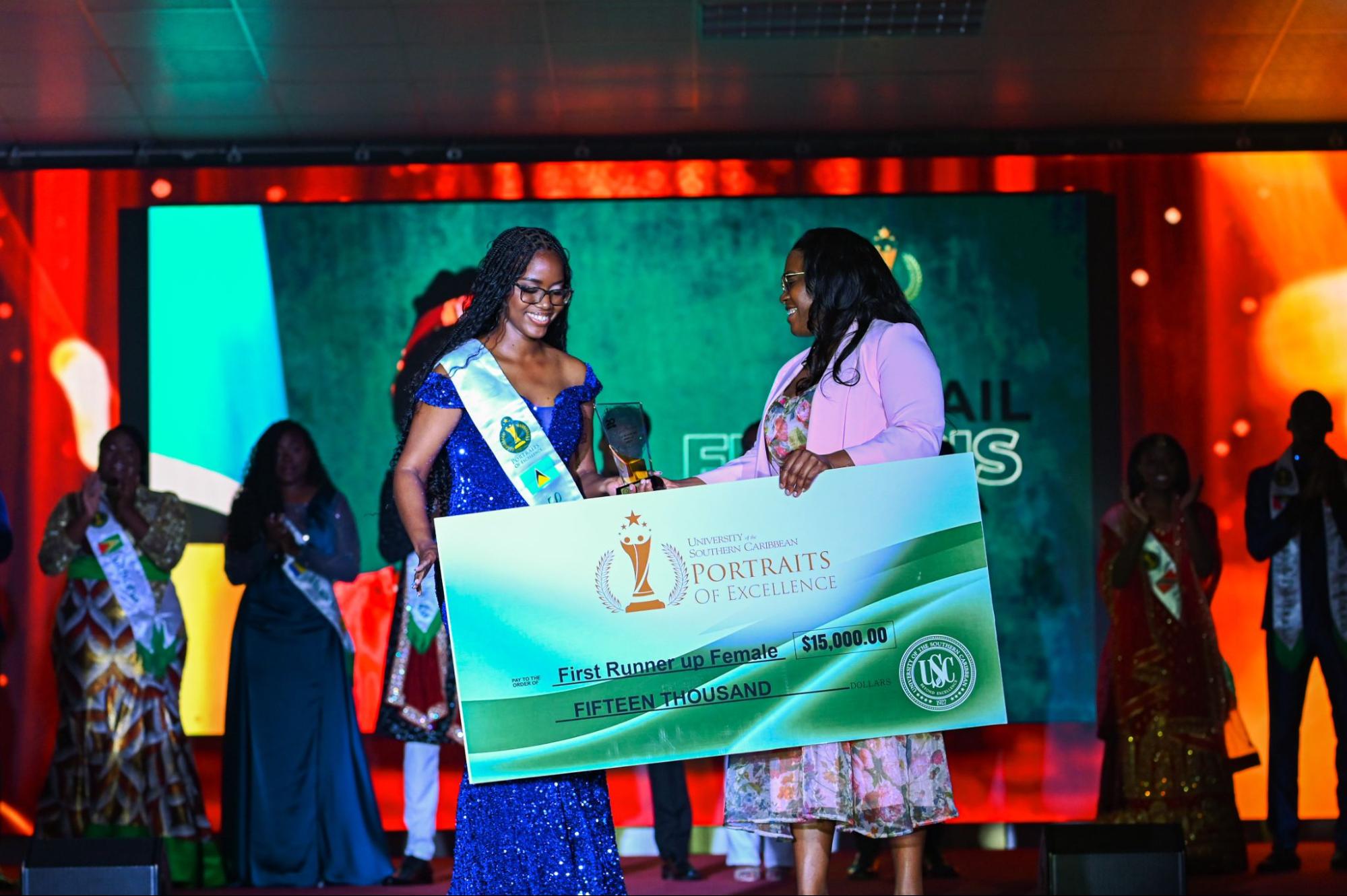 Abigail Francis, wearing a blue sequined gown, smiles as she is handed a large presentation cheque for fifteen thousand dollars for the First Runner-Up Female award.