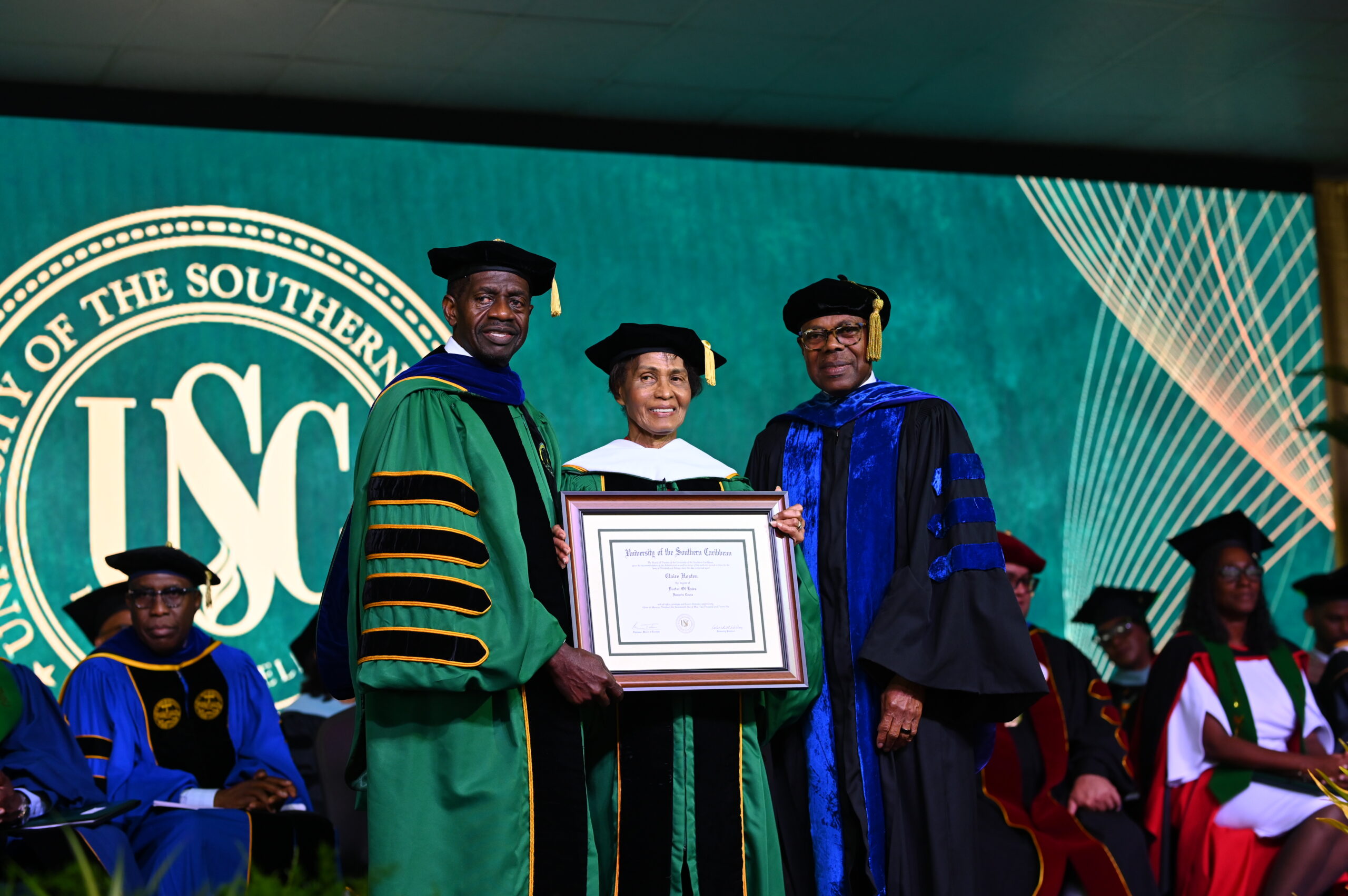 Mrs Claire Chunlan Aleong-Hosten smiles in the centre as she is presented with an honourary doctoral degree by Dr Colwick Wilson on the left and Dr Len Archer on the right.