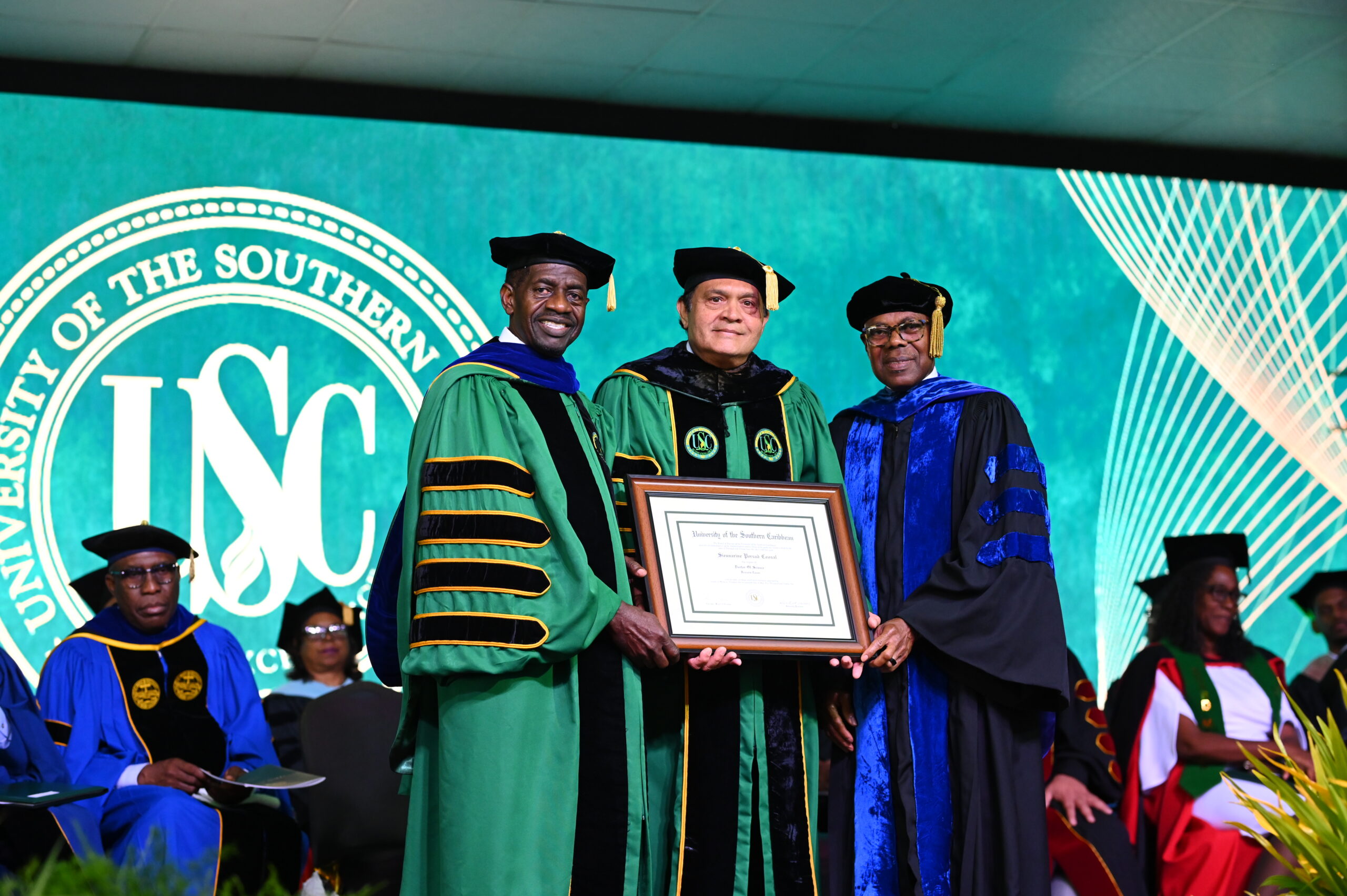 Dr Sieunarine Coosal stands in the centre in full academic dress as he is awarded an honourary doctorate by Dr Colwick Wilson on the left and Dr Len Archer on the right.