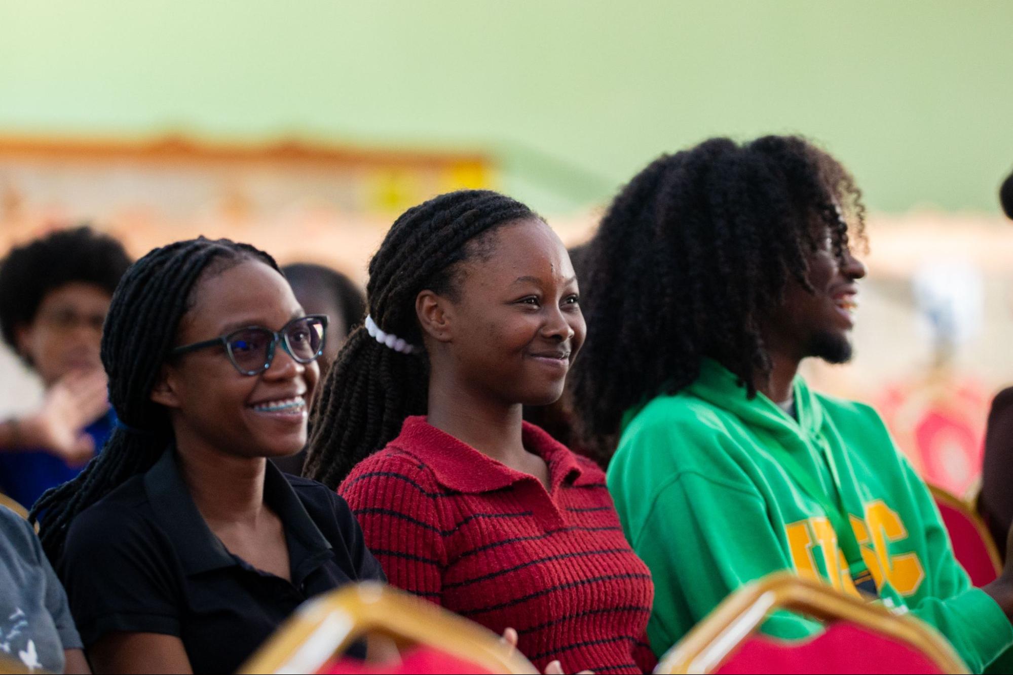 Three members of Team SPEAR sitting in the audience, including a woman with glasses and a man in a green USC hoodie, watching the debate attentively.