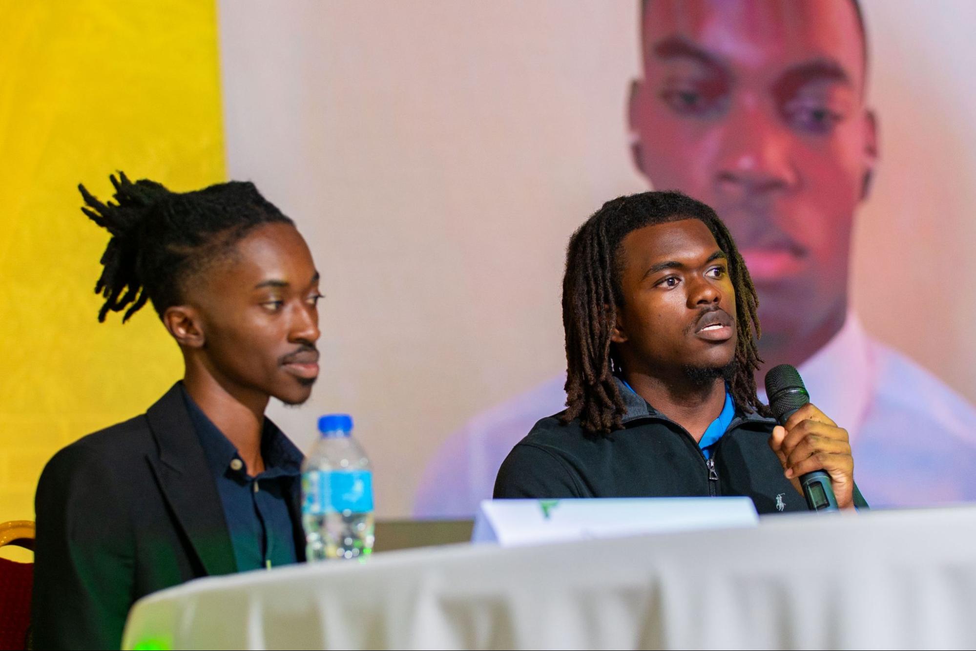 Dwayne Headley, Presidential candidate for Team SPEAR, speaks into a microphone at the debate table while Vice-Presidential candidate Marc Alleyne sits beside him.