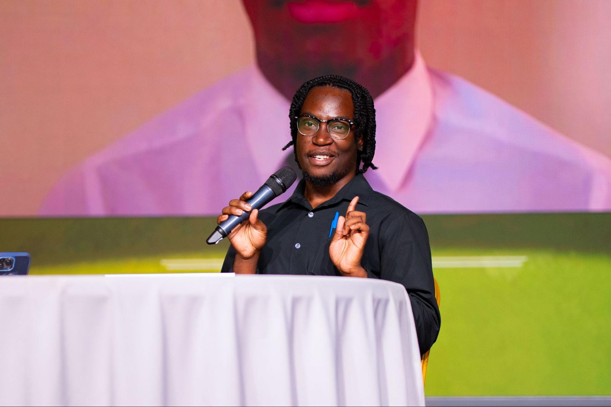 Ezekiel Oxley, an independent candidate for ASB President, smiles and gestures with one hand while holding a microphone during his presentation.