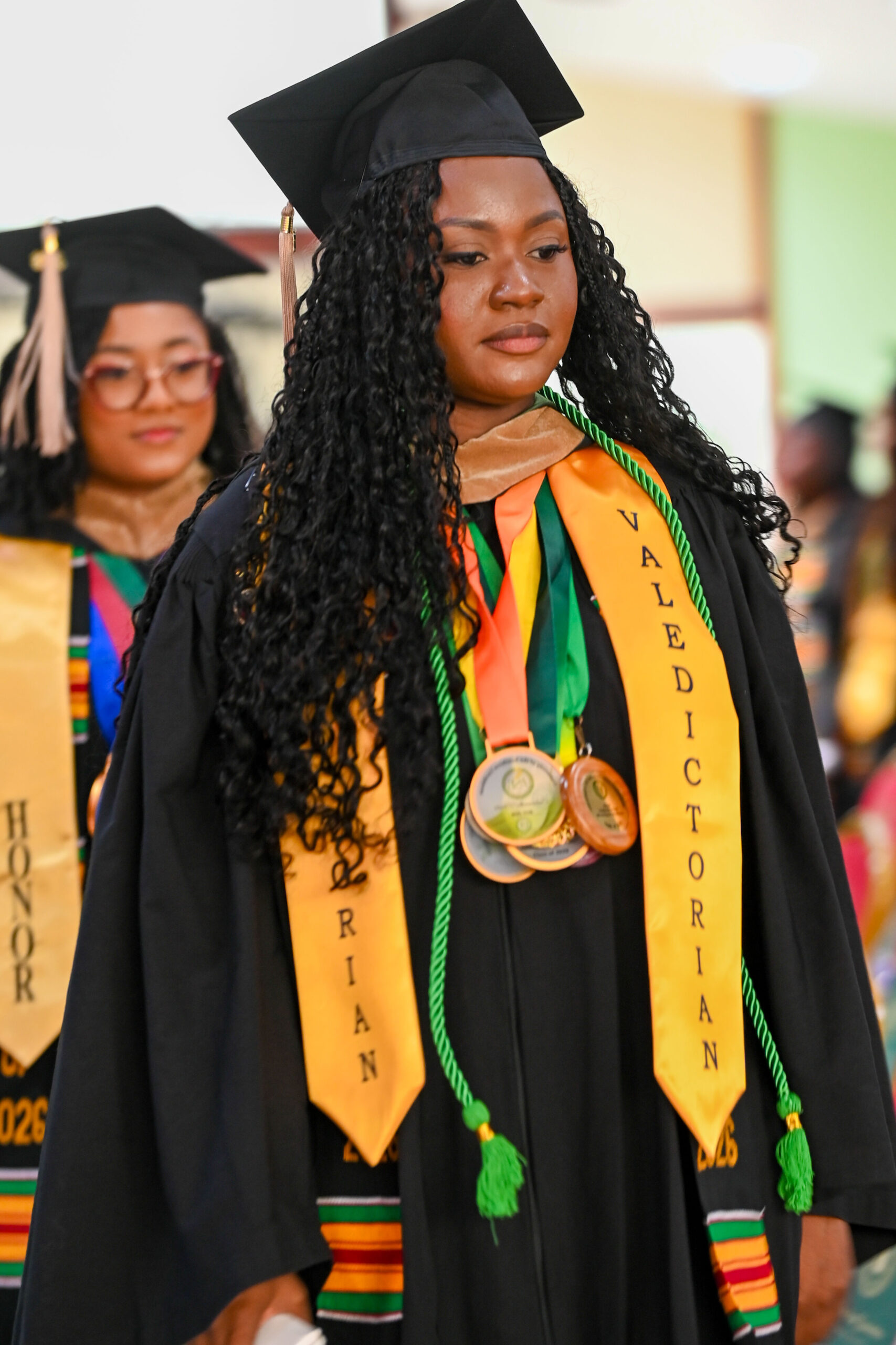 Ms Shafiya Castello, the Class of 2026 Valedictorian, smiling as she walks in the academic procession wearing her ceremonial sash and medals.