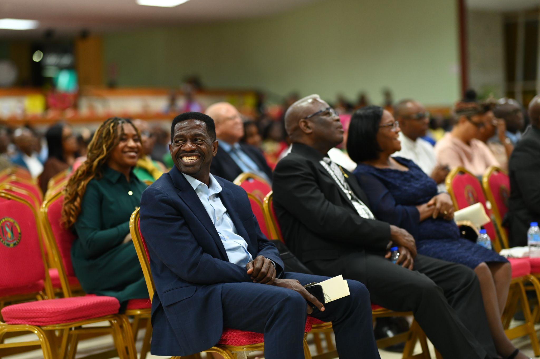 USC President Dr Colwick Wilson in a blue suit smiles broadly while seated in a red chair, with Dr Kern Tobias and other committee members seated beside him.