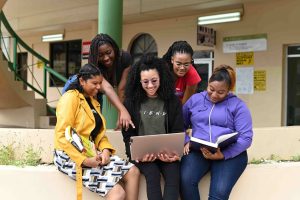 A diverse and engaged group of female students collaborating on a project together on campus, representing the dynamic programmes and collaborative student life at the University of the Southern Caribbean (USC).